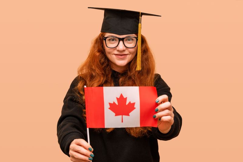 A graduate in cap and gown holding the Canadian flag