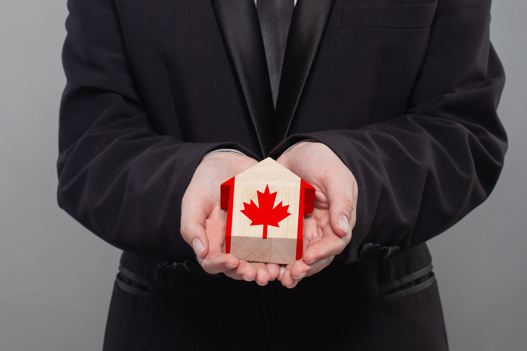 Hands holding a small wooden house with the Canadian flag