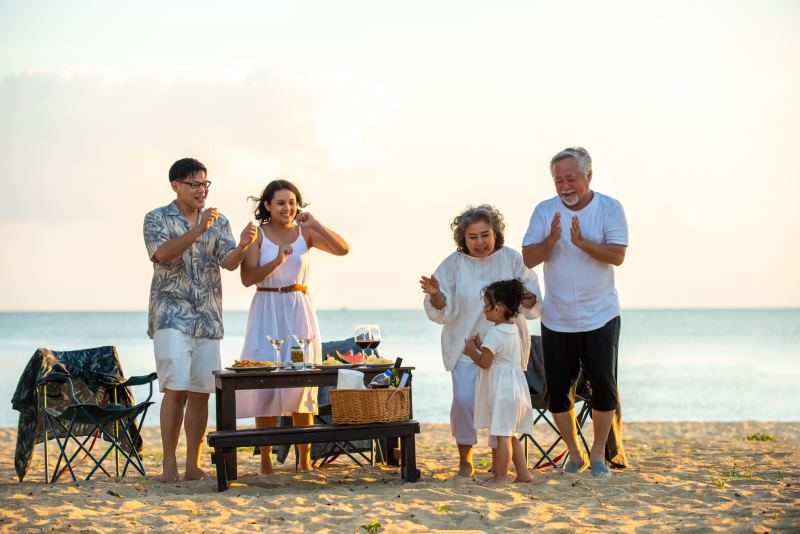 Three generations of a family dancing together on a beach at sunset