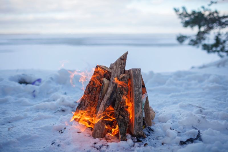 A family around a bonfire by a frozen lake in winter
